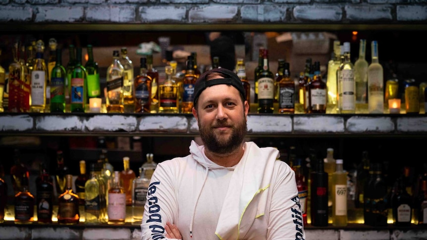 A man in a cap against a stocked bar