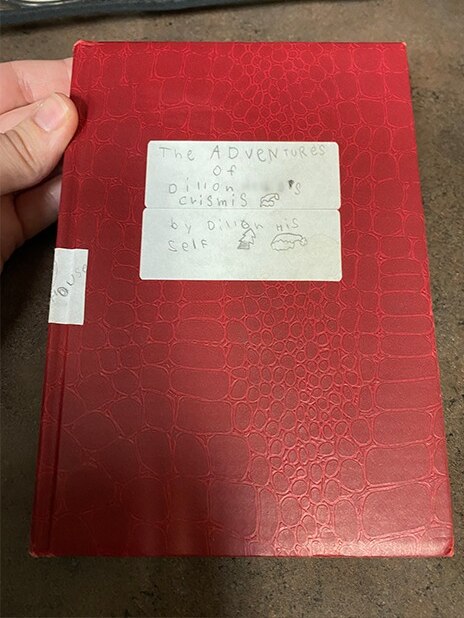 The cover and spine of a red leather journal are displated, with a sticker showing the title.