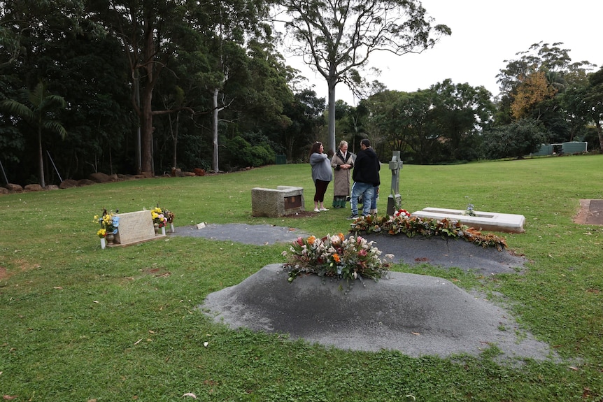 A long shot of a small group of people at a cemetery on an overcast day.