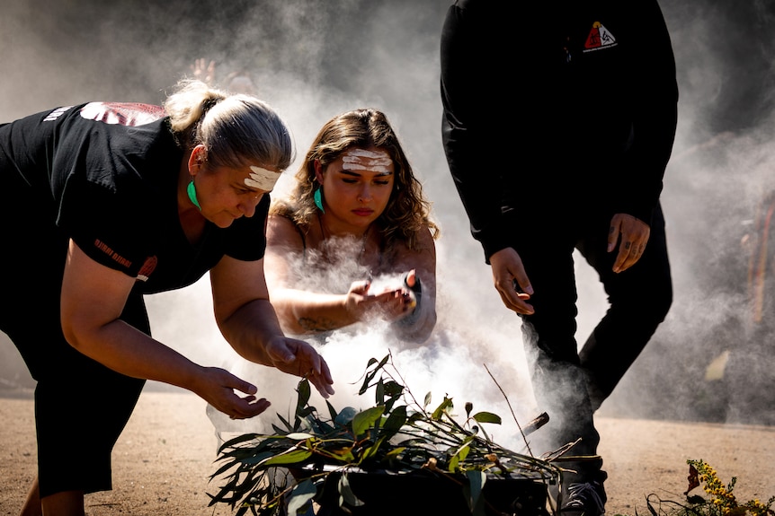 Two people drink the smoke from a vessel filled with leaves.