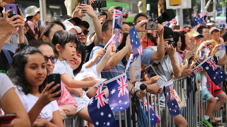 A crowd of people wave flags and take photos at Melbourne's Australia Day parade