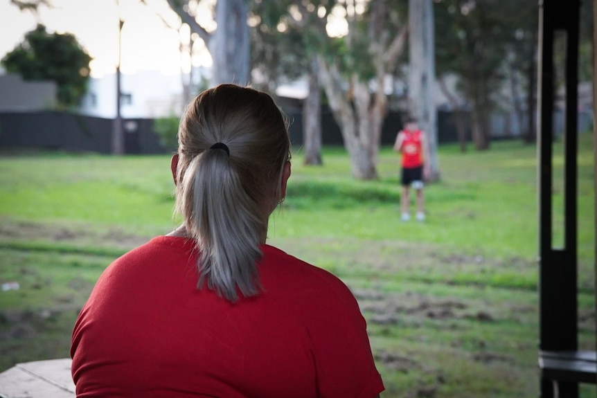 The back of a woman's head while she watches her son play sport in the background.