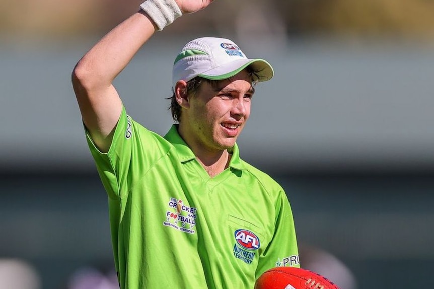 A young man in green umpire's shirt holds his arm up and readies to bounce the ball in AFL.