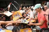 Tennis player Rafael Nadal smiles widely as he signs a poster for a fan in a crowded mall.