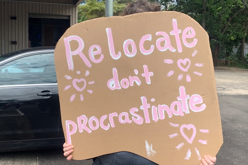 A homemade cardboard sign reads "Relocate don't procrastinate".