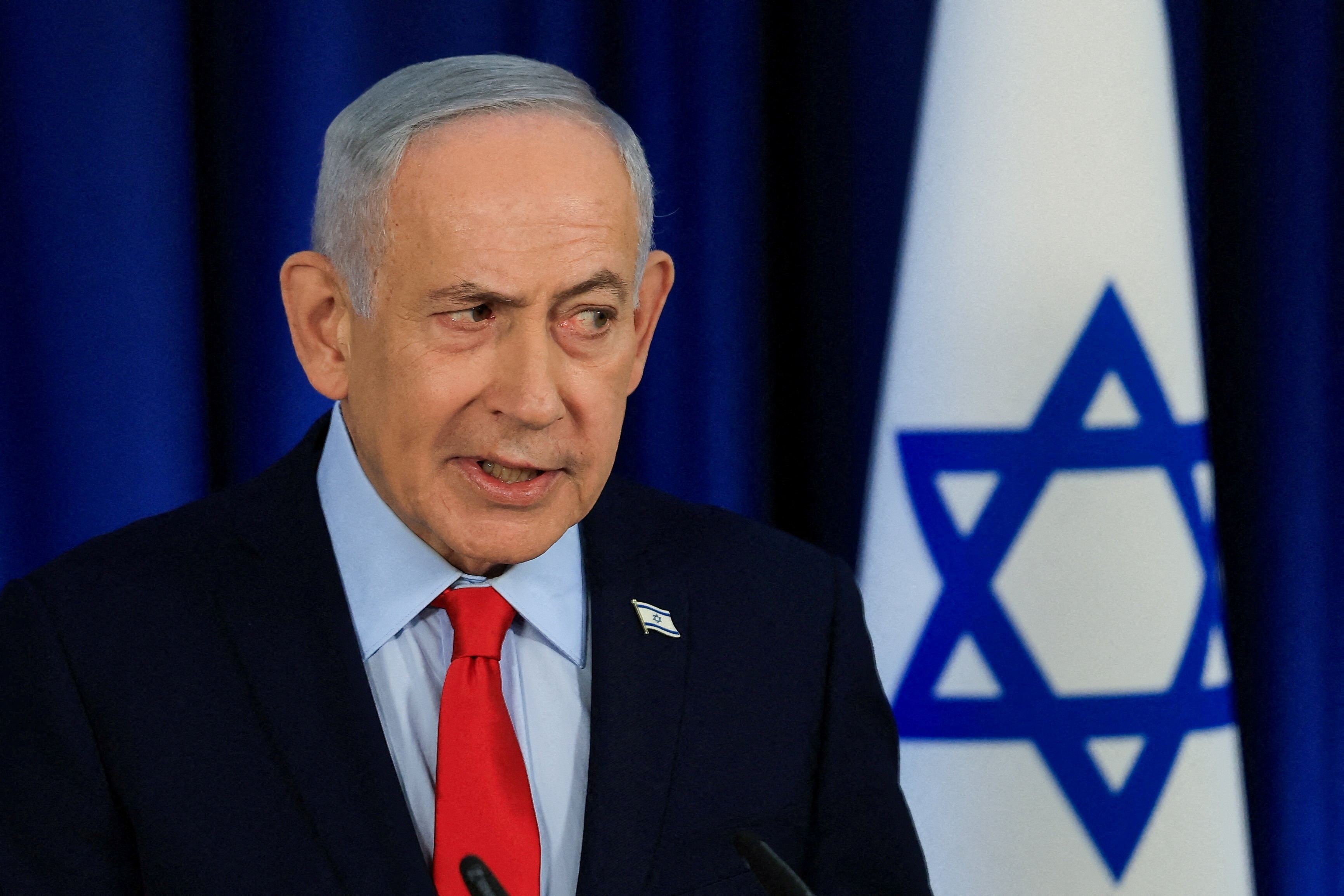 Benjamin Netanyahu at a press conference in front of an Israeli flag.