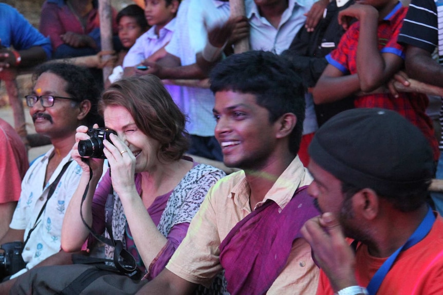 A woman with a canmera and a young man sit in a row of people watching a festival