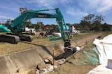A large excavator pulls up concrete from a channel.
