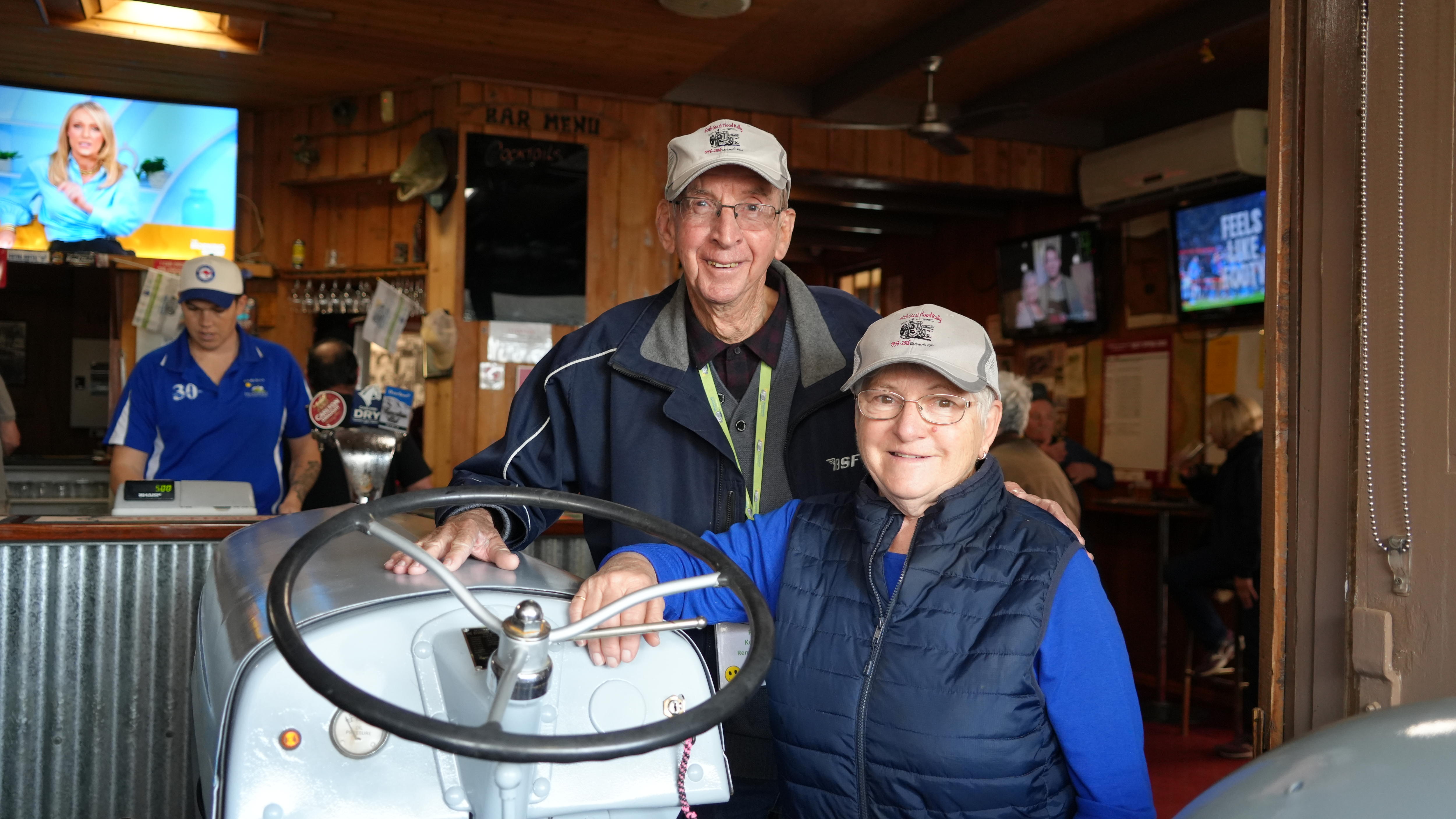 Una pareja de ancianos posa junto a un tractor que ha sido conducido hasta el frente del bar de un pub.