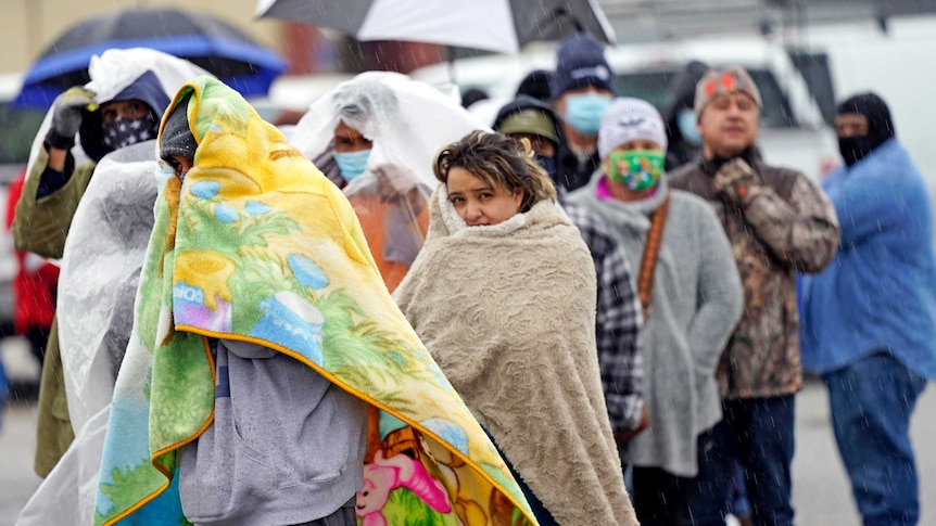 People wrapped in blankets wait in line to fill propane tanks