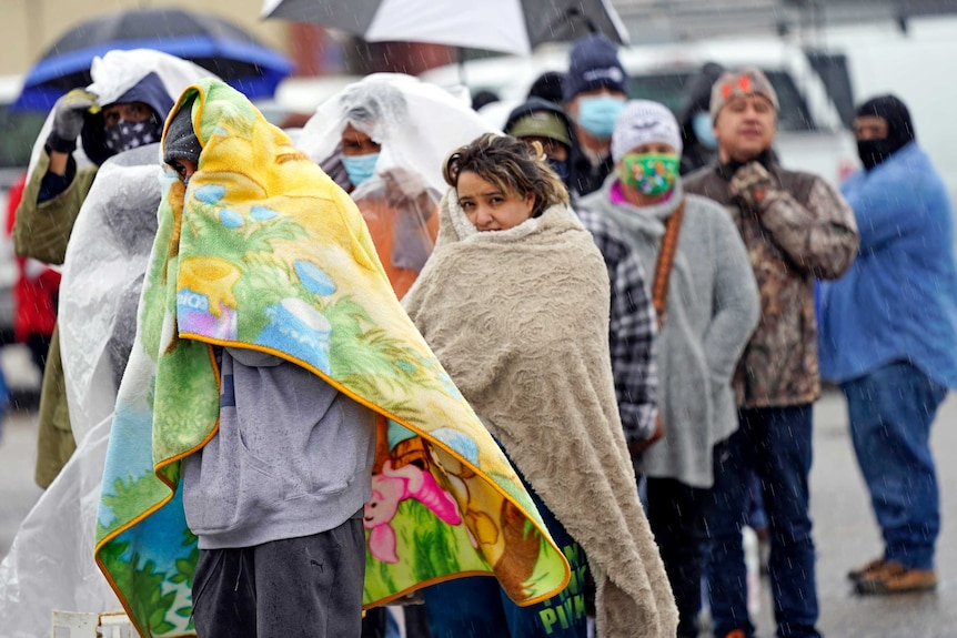 People wrapped in blankets wait in line to fill propane tanks