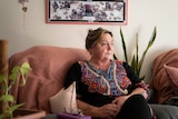 A woman sits in an armchair next to an indoor plant