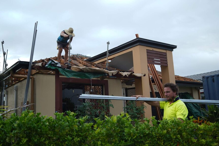 Roofers stand on top of the damaged roof of a house.
