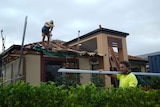 Roofers stand on top of the damaged roof of a house.