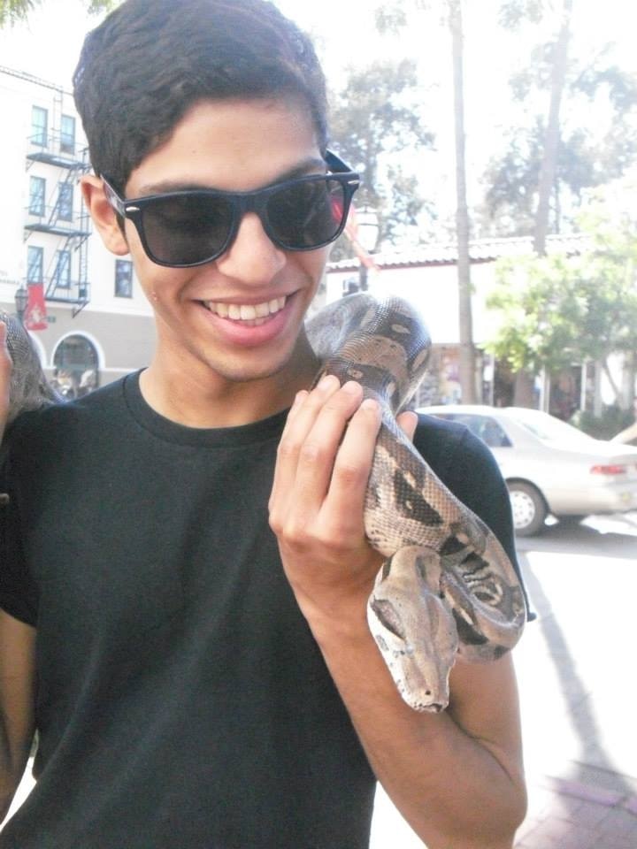 Comedian and writer AJ Lamarque poses with a snake while wearing sunglasses and a black t-shirt.