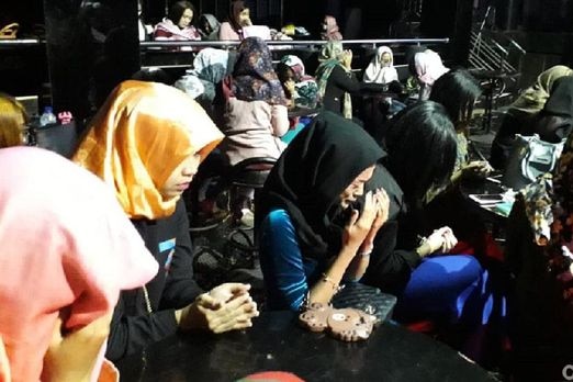 A veiled Islamic woman praying and crying surrounded by other veiled women