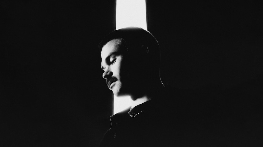 B&W headshot of Dom Dolla, taken from below as he looks down. His face is lit up with a white beam of light.