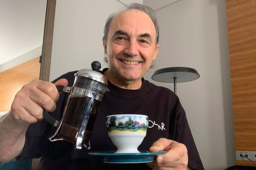 A man smiling with a cup of coffee.