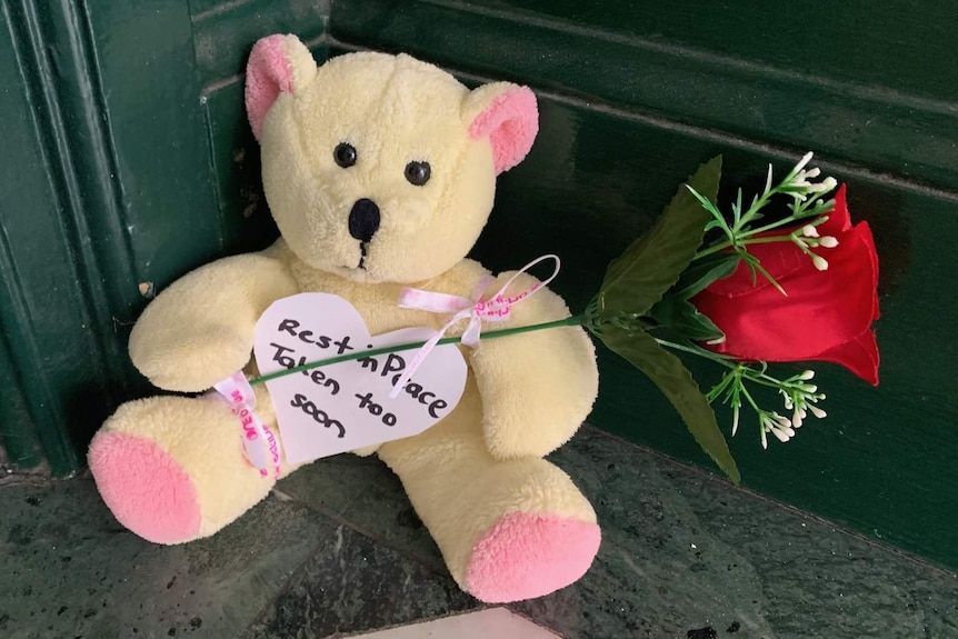 a teddy bear holding a rose with a note reading rest in peace taken too soon
