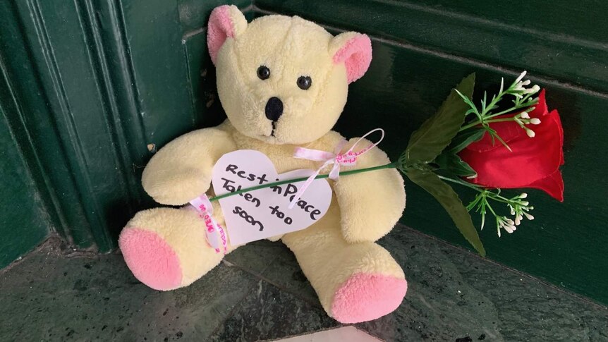 a teddy bear holding a rose with a note reading rest in peace taken too soon