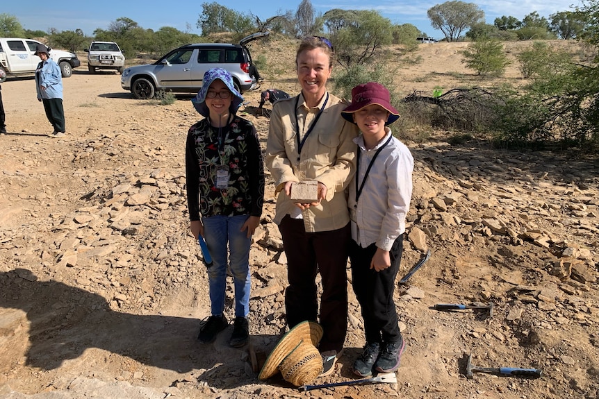 Tourists stand in outback holding a fossil. 
