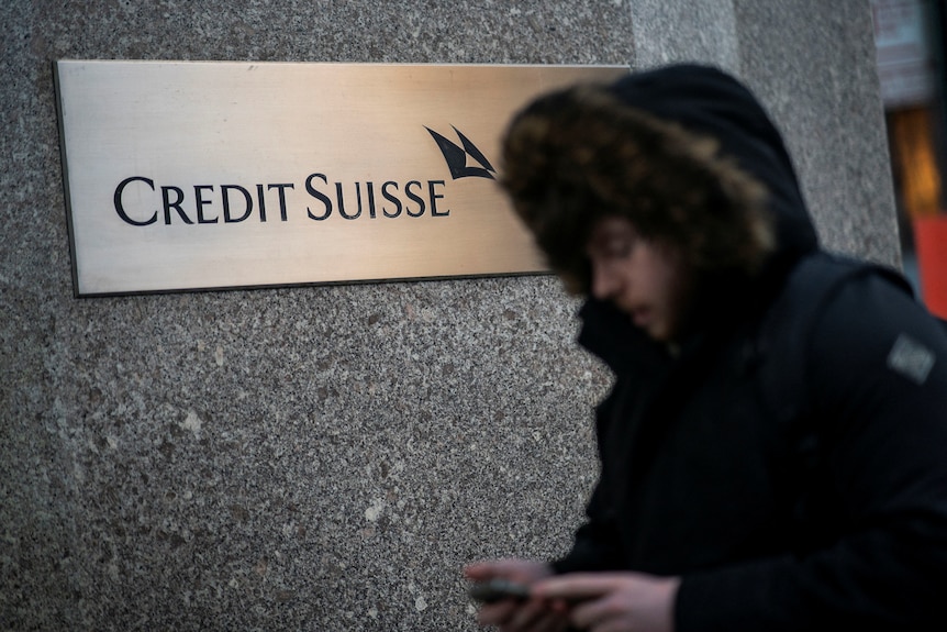 A man wearing a black hooded parka walks past a Credit Suisse sign.