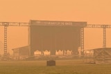 A stage sits alone on a field shrouded by an orange coloured sky.
