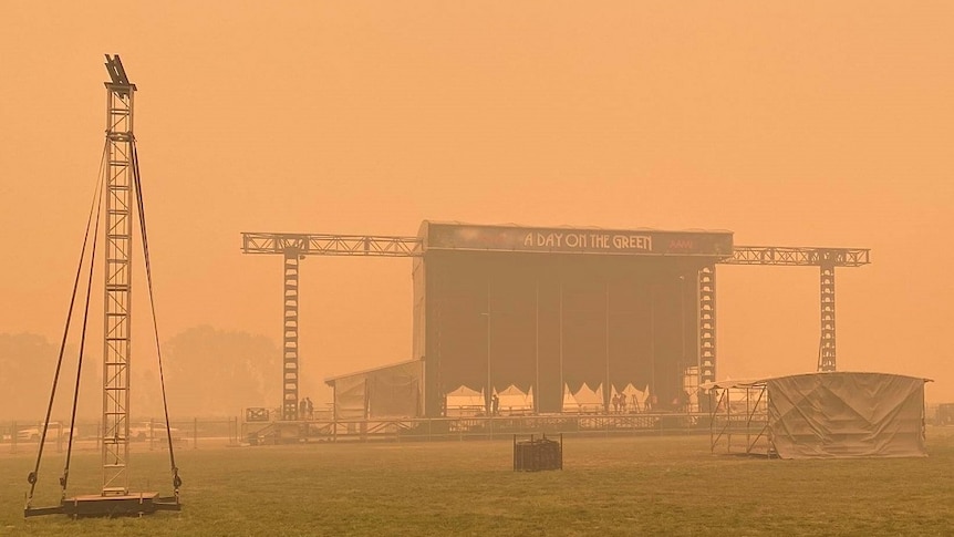 A stage sits alone on a field shrouded by an orange coloured sky.