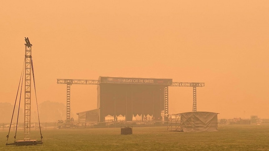 A stage sits alone on a field shrouded by an orange coloured sky.