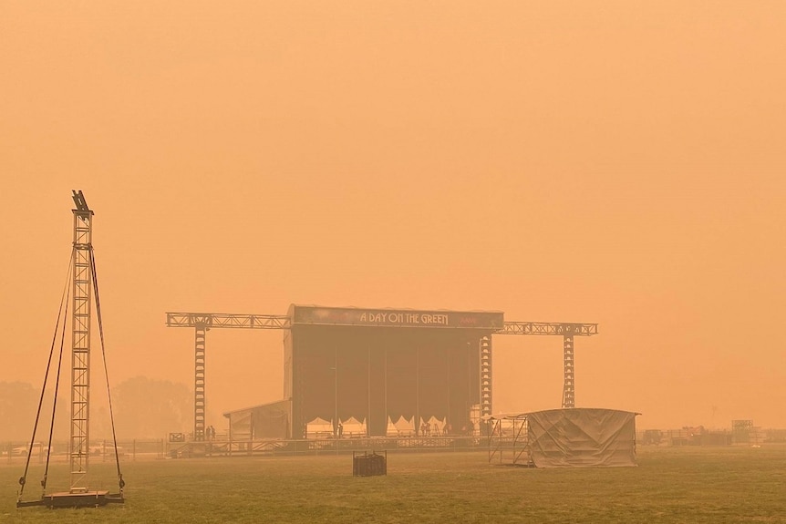 A stage sits alone on a field shrouded by an orange coloured sky.