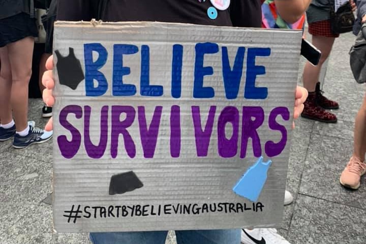 A woman holding a sign saying "Believe survivors"