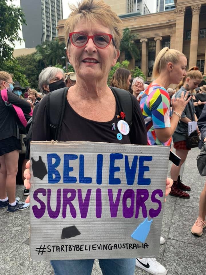 A woman holding a sign saying "Believe Survivors"