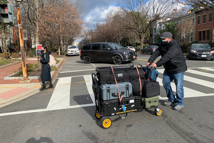 Man pushing trolley loaded high with camera equipment in cases on Washington street.