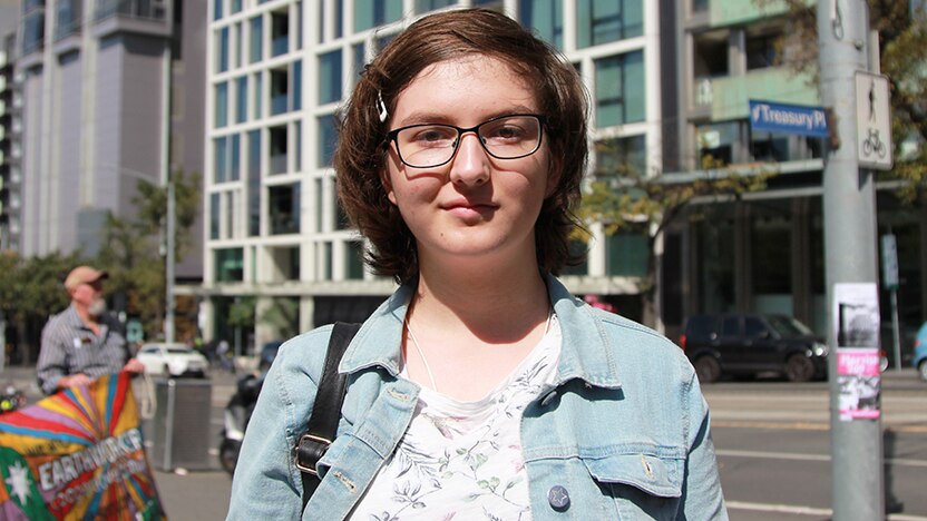 A 13-year-old girl in a denim jacket stands on a city street.