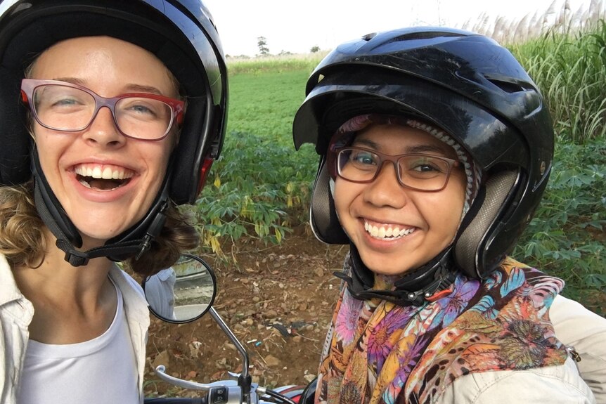 Two women wearing helmets smile at the camera.