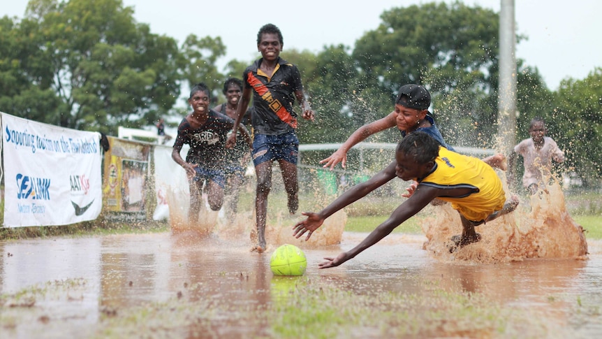 A group of kids dive for a football in a puddle on the Tiwi Islands.