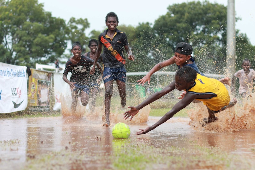 A group of kids dive for a football in a puddle on the Tiwi Islands.