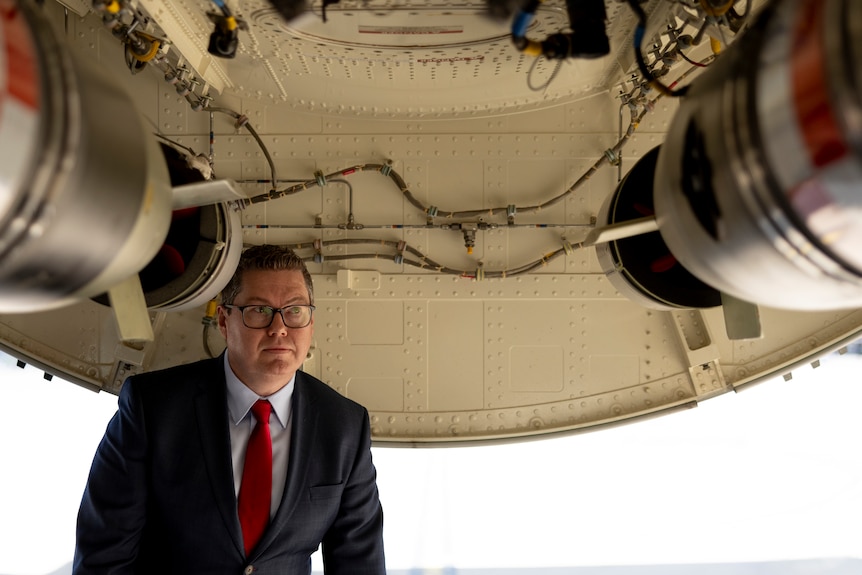 Pat Conroy wearing a suit and glasses, standing underneath airplane machinery