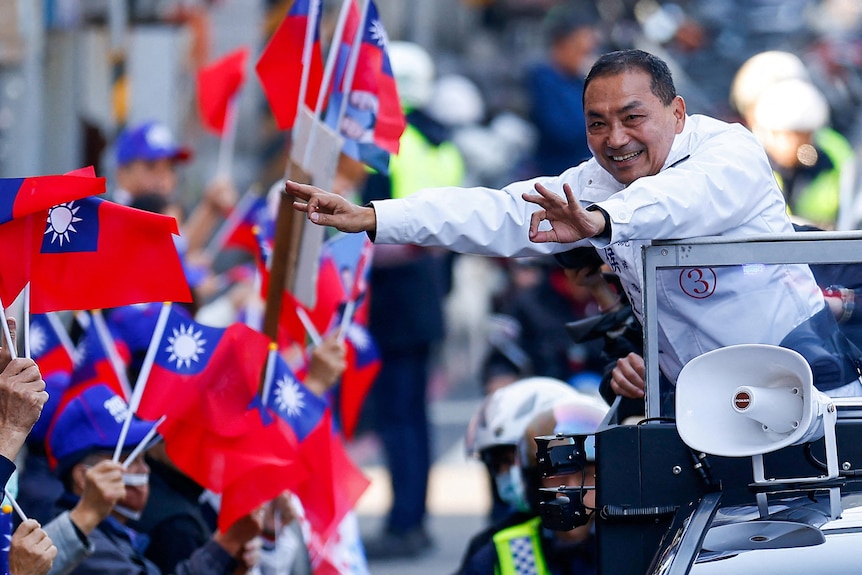 A man in a car smiles and waves at crowds.