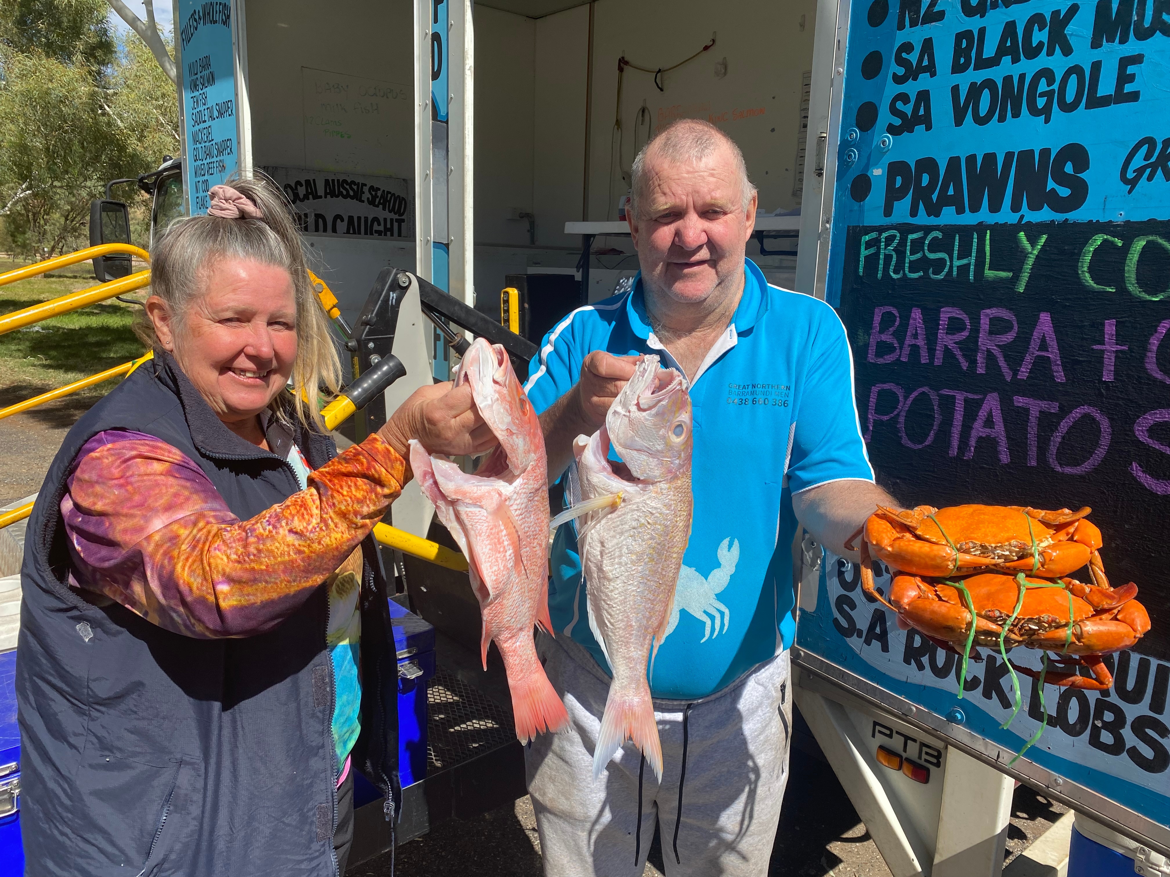 A woman, Lisa, holds a foot long fish, while her brother to  her left holds a fish in one hand and two mud crabs in the other.
