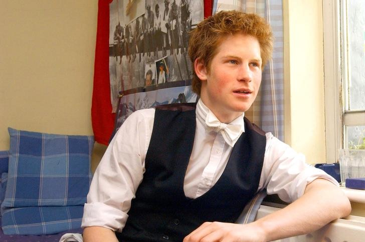 Prince Harry wears a waistcoat, shirt, trousers and bow tie as he leans against a radiator next to a window, looking to right.