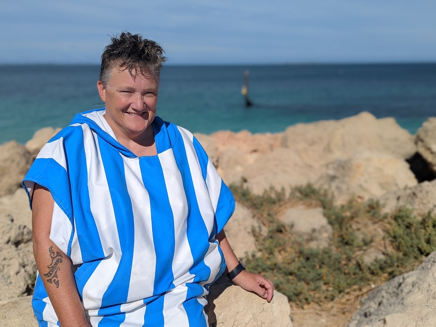 Woman in striped towel dress sitting on rocks in front of beach