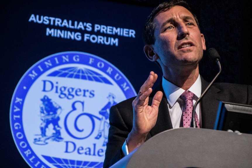 A mining executive speaking in a suit from a podium with a microphone at a business conference