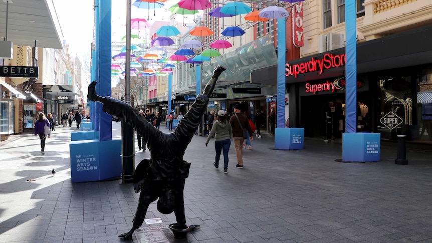 A shopping mall in Perth with an art installation of colourful umbrellas suspended in the air and a statue of a man handstanding