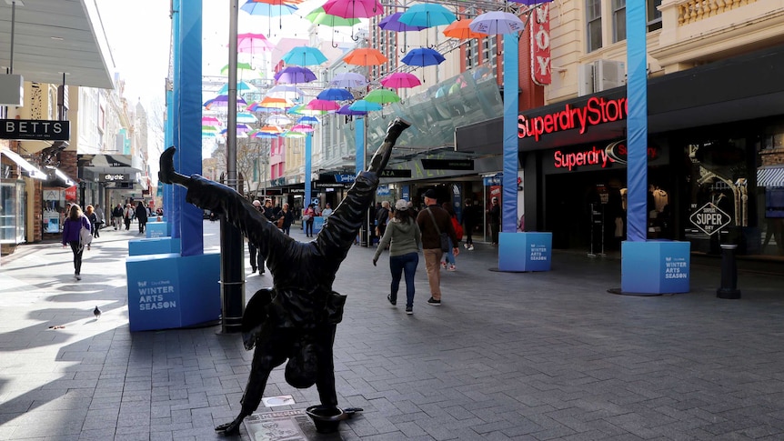 A shopping mall in Perth with an art installation of umbrellas suspended in the air and a statue of a man handstanding.