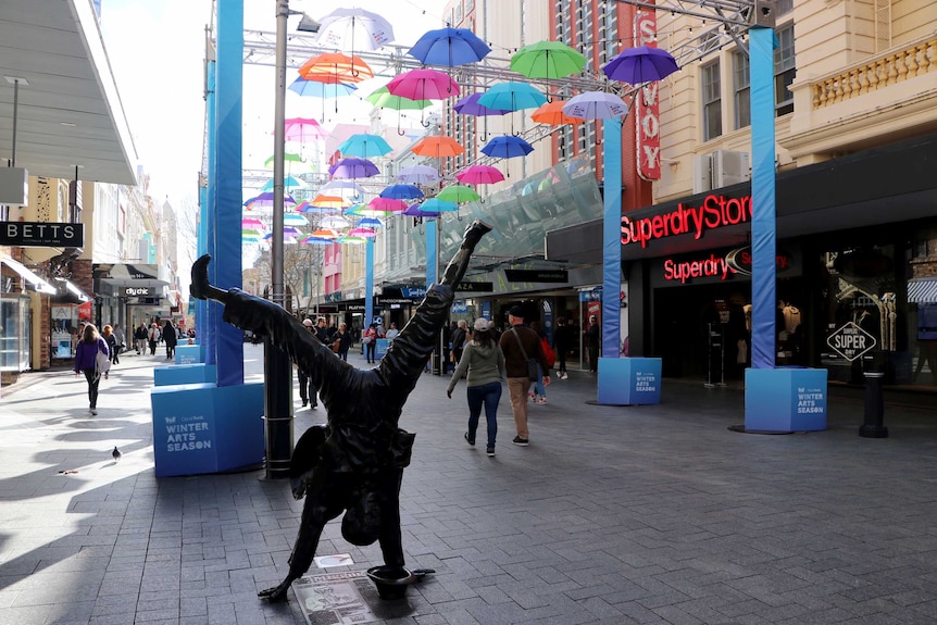 A shopping mall in Perth with an art installation of umbrellas suspended in the air and a statue of a man handstanding.