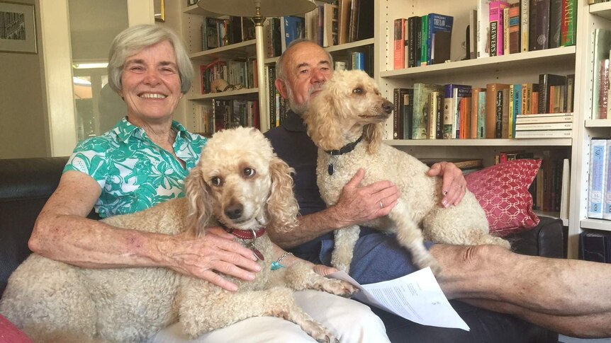 Frances Rose and her husband sit together on the lounge with a pet dog on each of their laps.