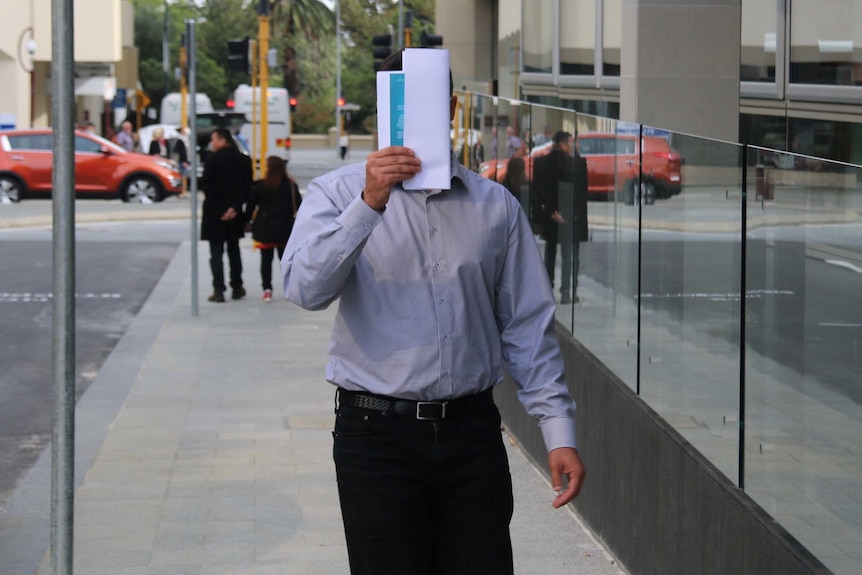 Iman holds a piece of paper in front of his face as he walks in front of a court.