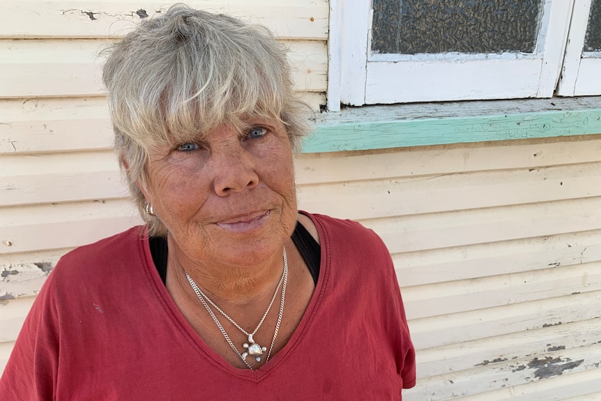 a close-up picture of a woman with a serious expression, she has short grey hair and is wearing silver necklaces