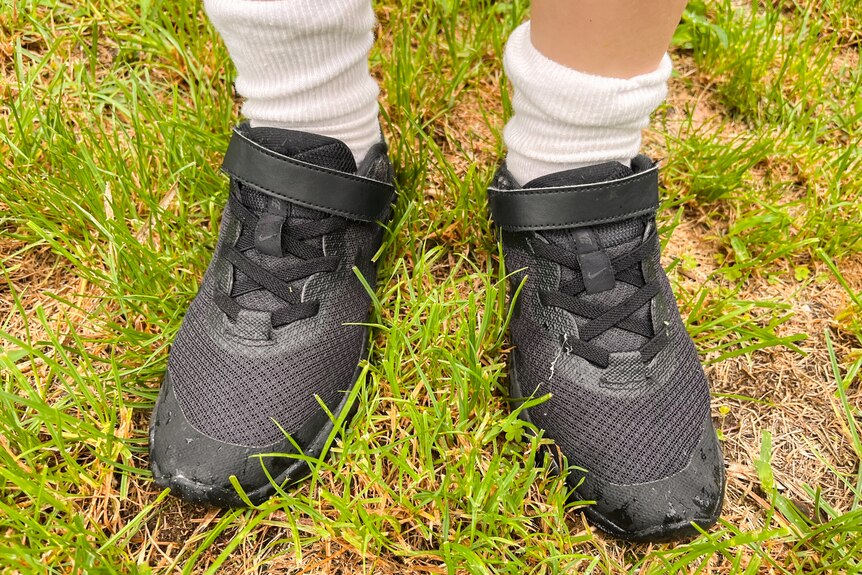 A close-up of a child's black school shoes being worn the wrong way around.
